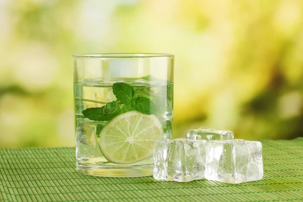 Glass of water with ice, mint and lime on table on bright background — Stock Photo, Image