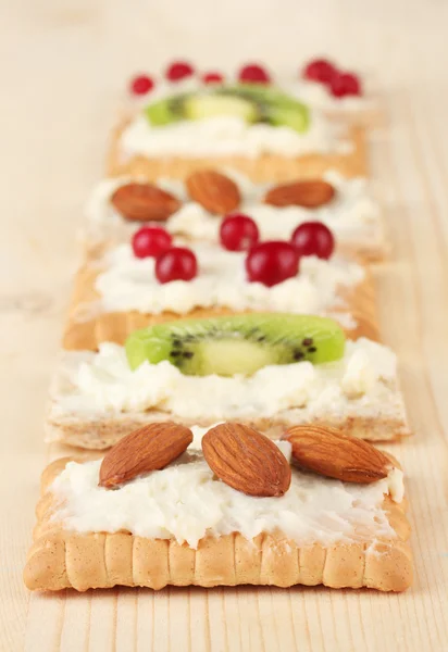 Tasty canapes with cheese, kiwi and cranberry, almond, on wooden background — Stock Photo, Image