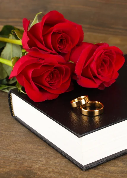 Wedding rings on bible with roses on wooden background — Stock Photo, Image