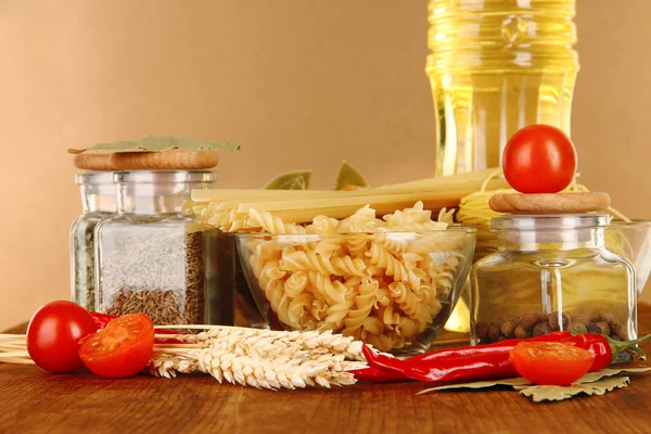 Diferentes tipos de pasta, especias, tomates sobre una mesa de madera sobre fondo marrón — Foto de Stock