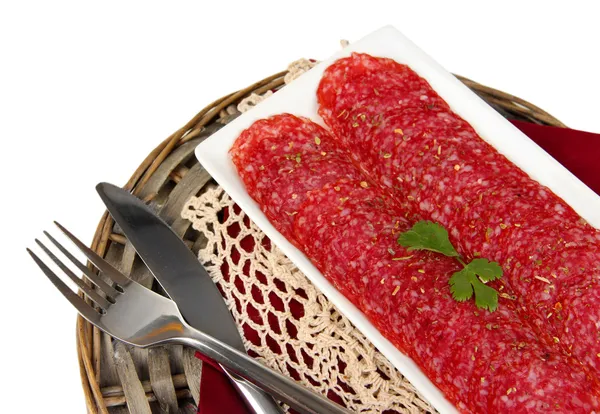 Tasty salami on plate on wicker cradle isolated on white — Stock Photo, Image