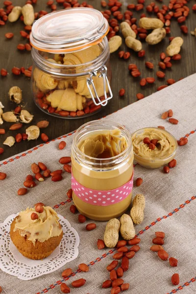 Delicious peanut butter in jar with baking on napkin on wooden table close-up — Stock Photo, Image