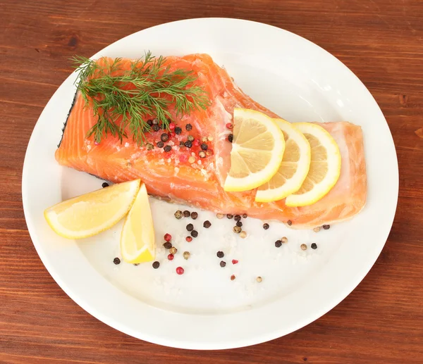Fresh salmon fillet with herbals and lemon slices on plate,on wooden background — Stock Photo, Image