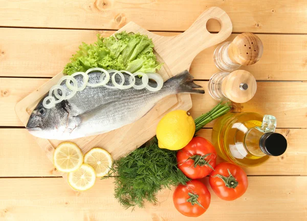 Fresh dorado on chopping board with lemon and vegetables on wooden table — Stock Photo, Image