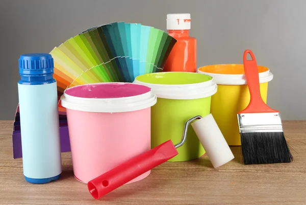 Farby garnki, pędzle i kolorowe próbki na drewnianym stole na szarym tle — Zdjęcie stockowe