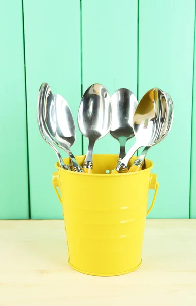 Spoons in metal bucket on color wooden background — Stock Photo, Image