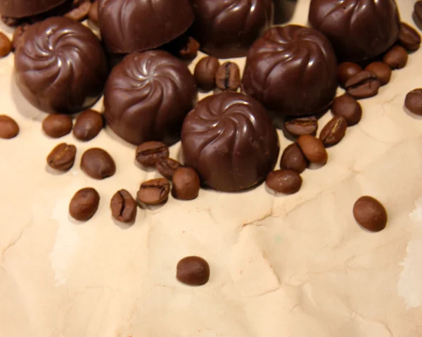 Chocolade snoepjes en koffie bonen, op beige papier achtergrond — Stockfoto