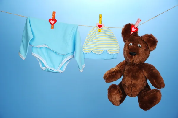 Vêtements bébé suspendus sur corde à linge, sur fond bleu — Photo