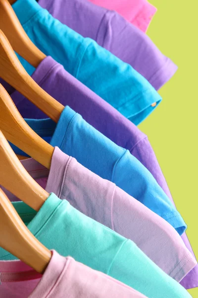 Lots of T-shirts on hangers on green background — Stock Photo, Image