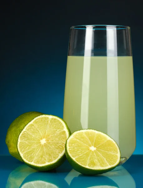 Delicious lemon juice in glass and limes next to it on dark blue background — Stock Photo, Image