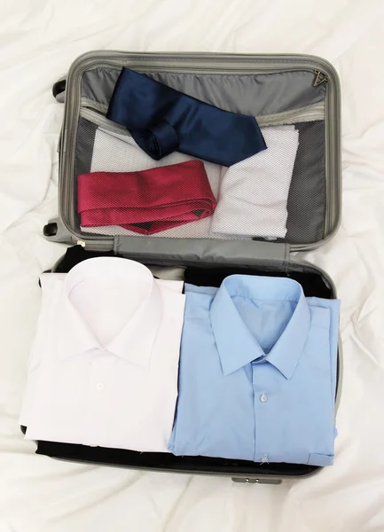 Otevřít šedý kufr s oblečením na posteli — Stock fotografie