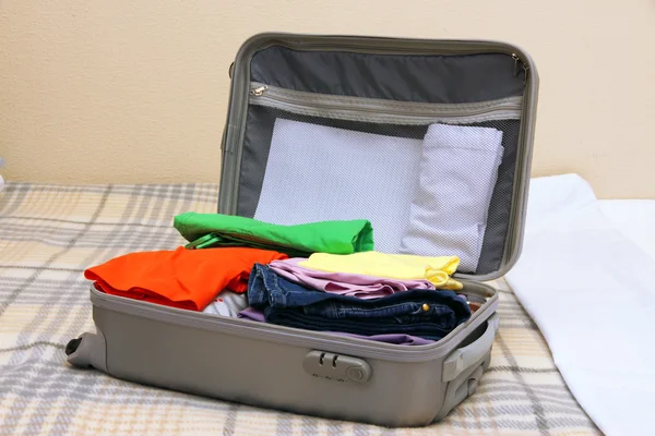 Valise ouverte grise avec vêtements sur le lit — Photo