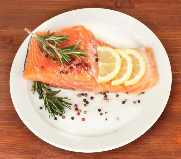 Frisches Lachsfilet mit Kräutern und Zitronenscheiben auf Teller, auf Holzgrund — Stockfoto