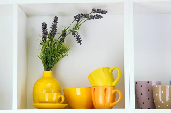 Prateleiras brancas bonitas com utensílios de mesa e deco — Fotografia de Stock