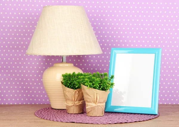 Colorful photo frame, lamp and flowers on wooden table on lilac polka dots background — Stock Photo, Image
