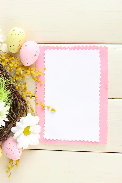 Пустая открытка с пасхальными яйцами и цветами мимозы на белом деревянном фоне — стоковое фото