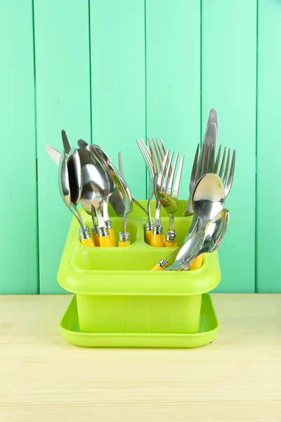 Knives, spoons, forks in plastic container for drying, on color wooden background — Stock Photo, Image