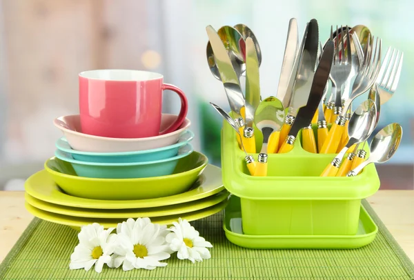 Placas, tenedores, cuchillos, cucharas y otros utensilios de cocina sobre estera de bambú, sobre fondo brillante —  Fotos de Stock