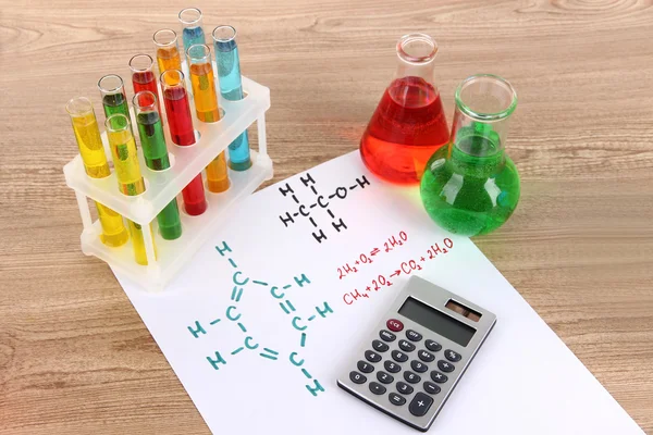 Reagenzgläser mit bunten Flüssigkeiten und Formeln auf dem Tisch — Stockfoto