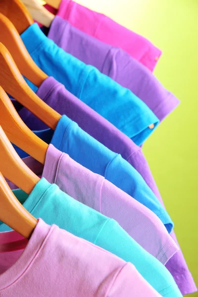 Lots of T-shirts on hangers on green background — Stock Photo, Image