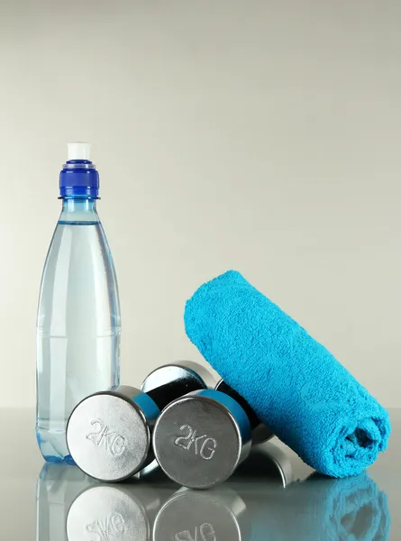 Halteres com toalha e garrafa de água sobre fundo cinza — Fotografia de Stock