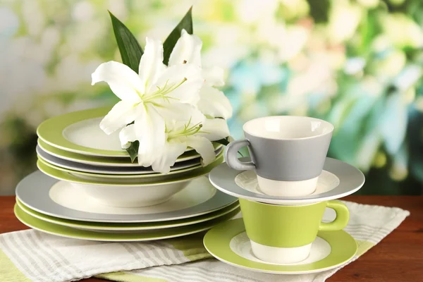 Empty plates and cups on wooden table on green background — Stock Photo, Image