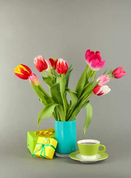 Красивые тюльпаны в ведре с подарками и чашкой чая на сером фоне — стоковое фото