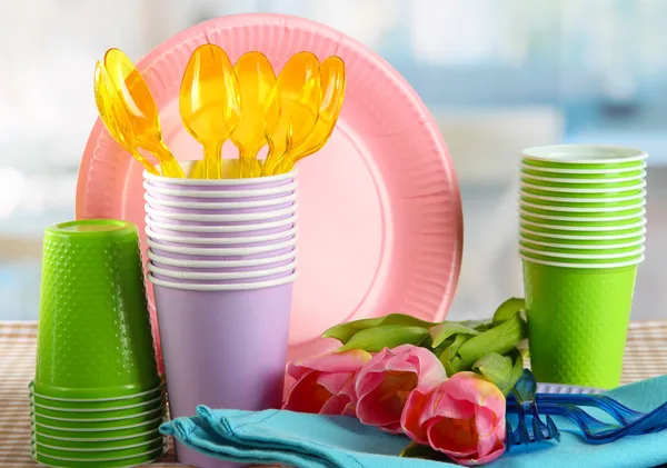 Louça de mesa de plástico multicolorido na mesa com tulipas de perto — Fotografia de Stock