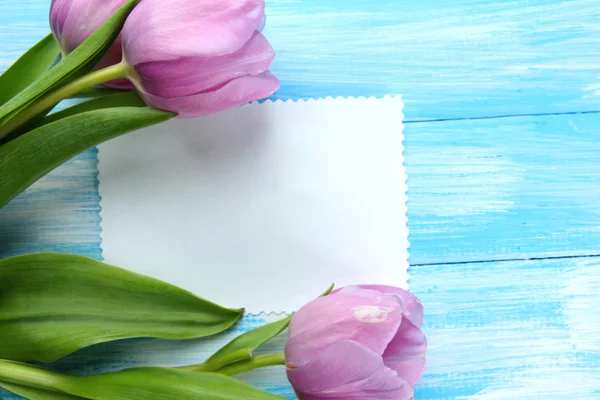 Schöner Strauß lila Tulpen und leere Karte auf blauem Holzhintergrund — Stockfoto