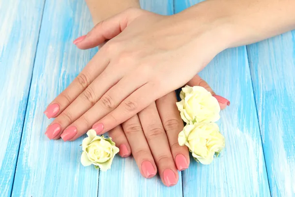 Mãos de mulher com manicure rosa e flores, na cor de fundo de madeira — Fotografia de Stock