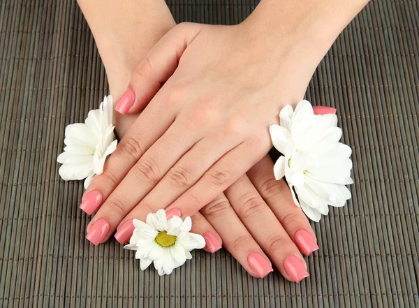 Mãos de mulher com manicure rosa e flores, em fundo tapete de bambu — Fotografia de Stock