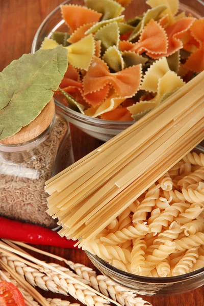 Diversi tipi di pasta, spezie, pomodori su un tavolo di legno — Foto Stock