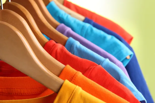 Lots of T-shirts on hangers on green background — Stock Photo, Image