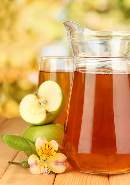 Полный стакан и кувшин яблочного сока и яблок на деревянном столе под открытым небом — стоковое фото