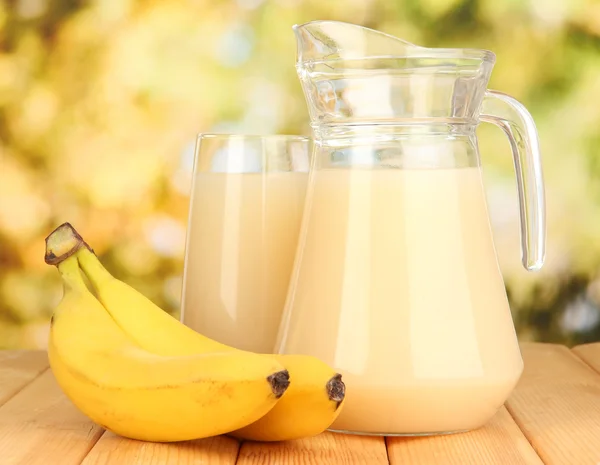 Fullt glas och kanna banana juice och bananer på träbord utomhus — Stockfoto