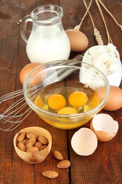 Zerbrochenes Ei in Schüssel und verschiedene Zutaten daneben auf Holztisch in Großaufnahme — Stockfoto
