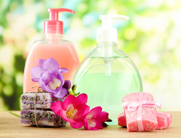 Liquid and hand-made soaps on wooden table, on green background