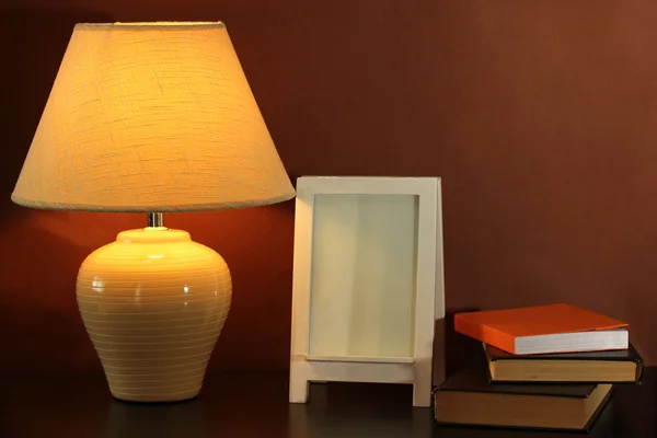 Weißer Fotorahmen und Lampe auf Holztisch auf braunem Wandhintergrund — Stockfoto