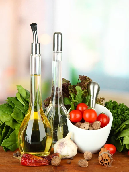 Composition of mortar, bottles with olive oil and vinegar, and green herbals, on bright background — Stock Photo, Image