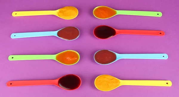 Baby puree in spoons on purple background — Stock Photo, Image