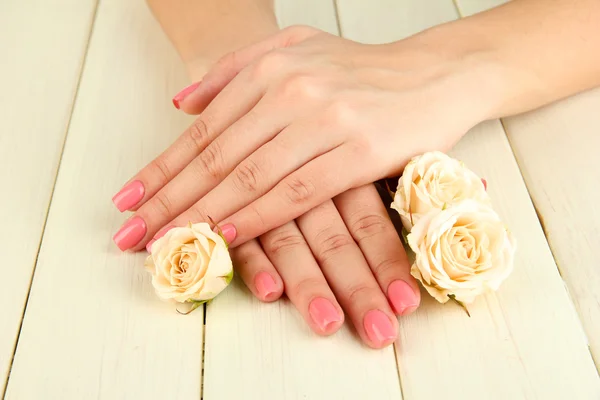 Frauenhände mit rosa Maniküre und Blumen, auf hölzernem Hintergrund — Stockfoto