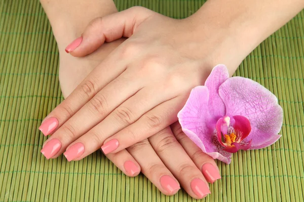 Frauenhände mit rosa Maniküre und Orchidee auf Bambusmatte Hintergrund — Stockfoto