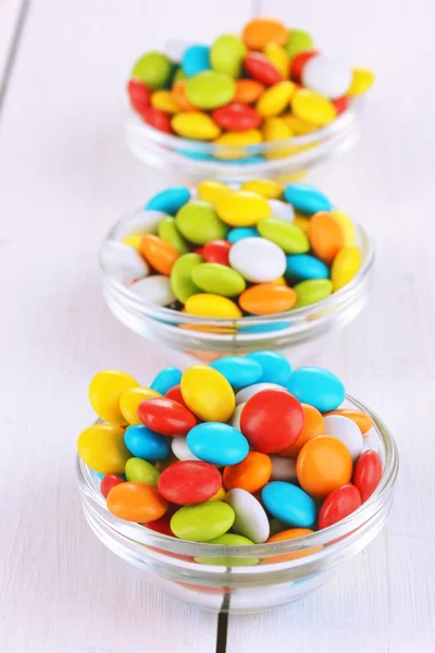 Coloridos caramelos en cuencos de vidrio sobre fondo blanco de madera — Foto de Stock