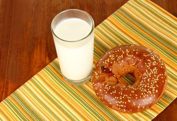 Broodje en een glas melk op servet op houten tafel — Stockfoto