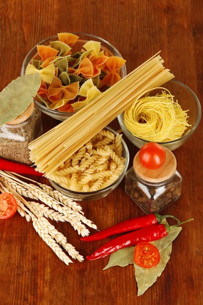 Diversi tipi di pasta, spezie, pomodori su un tavolo di legno — Foto Stock