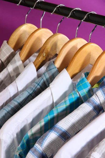 Camisas masculinas em cabides no fundo roxo — Fotografia de Stock