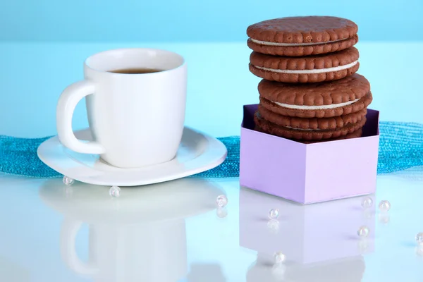 Choklad cookies med krämig skikt och kopp kaffe på blå bakgrund — Stockfoto