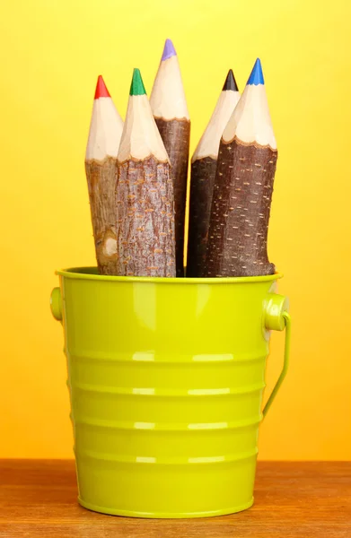 Colorful wooden pencils in pail on wooden table on yellow background — Stock Photo, Image