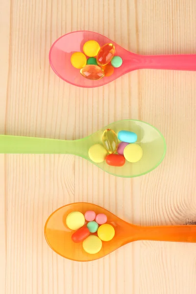 Plastic spoons with color pills on wooden background — Stock Photo, Image