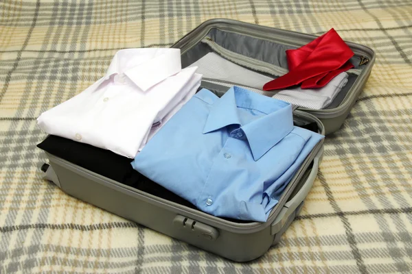 Offener grauer Koffer mit Kleidung auf Karo — Stockfoto